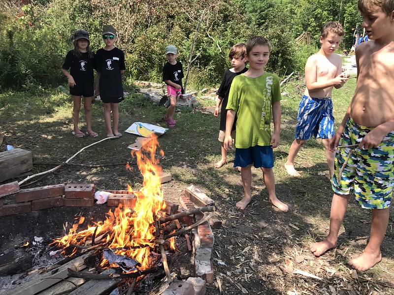 Barefoot Students standing around a fire they created at Forest School